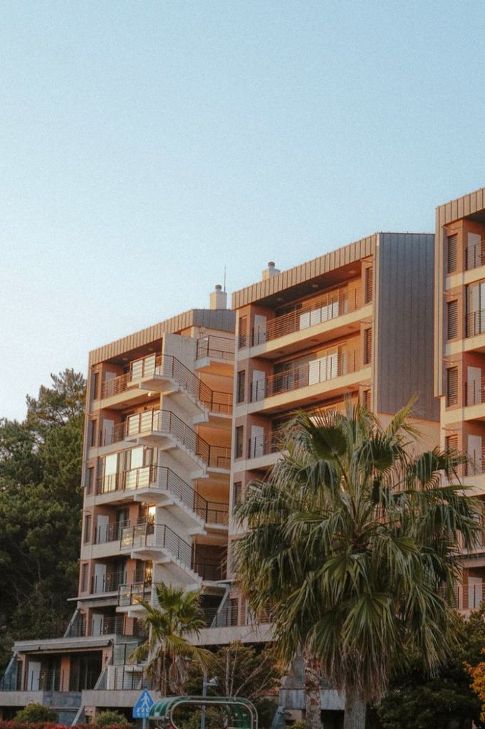 A contemporary apartment complex surrounded by palm trees at sunset, exuding a warm and inviting atmosphere.