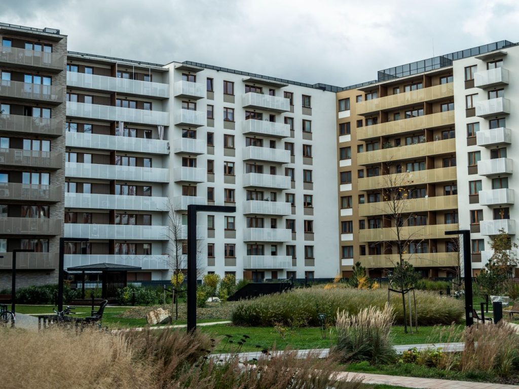 A modern apartment building surrounded by landscaped greenery under a cloudy sky.